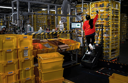 An Amazon employee sorts items into the waiting robots at the company’s facility on Staten Island in New York. (Chang W. Lee/The New York Times, 2021)