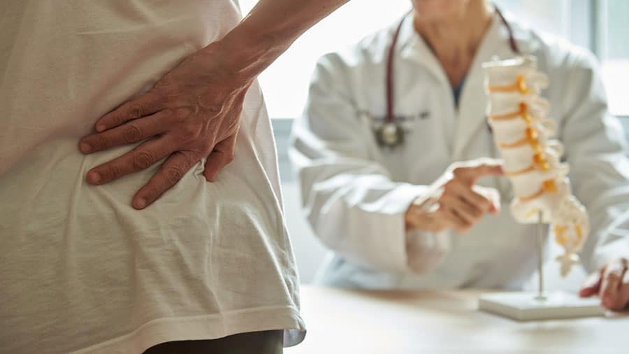 A doctors illustrates back pain on a model spine.