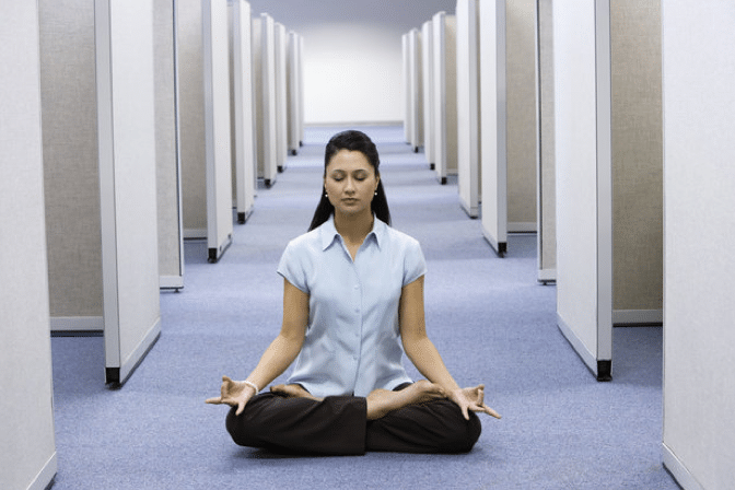 woman sitting in between office cubes meditating