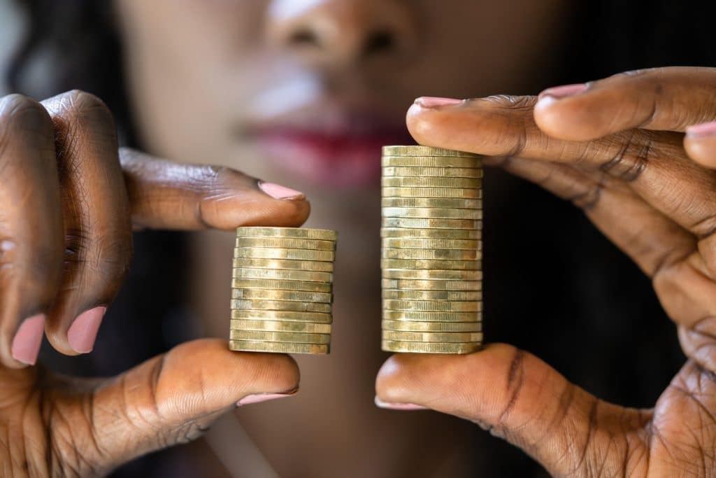 Black woman holds two unequal stacks of gold coins in her fingers to illustrate wage gap - Equal Pay Employment Attorneys Emery Reddy