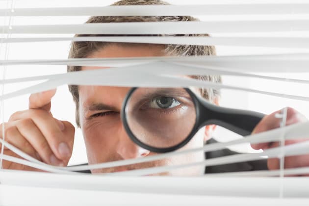 Businessman peeking through blinds with magnifying glass