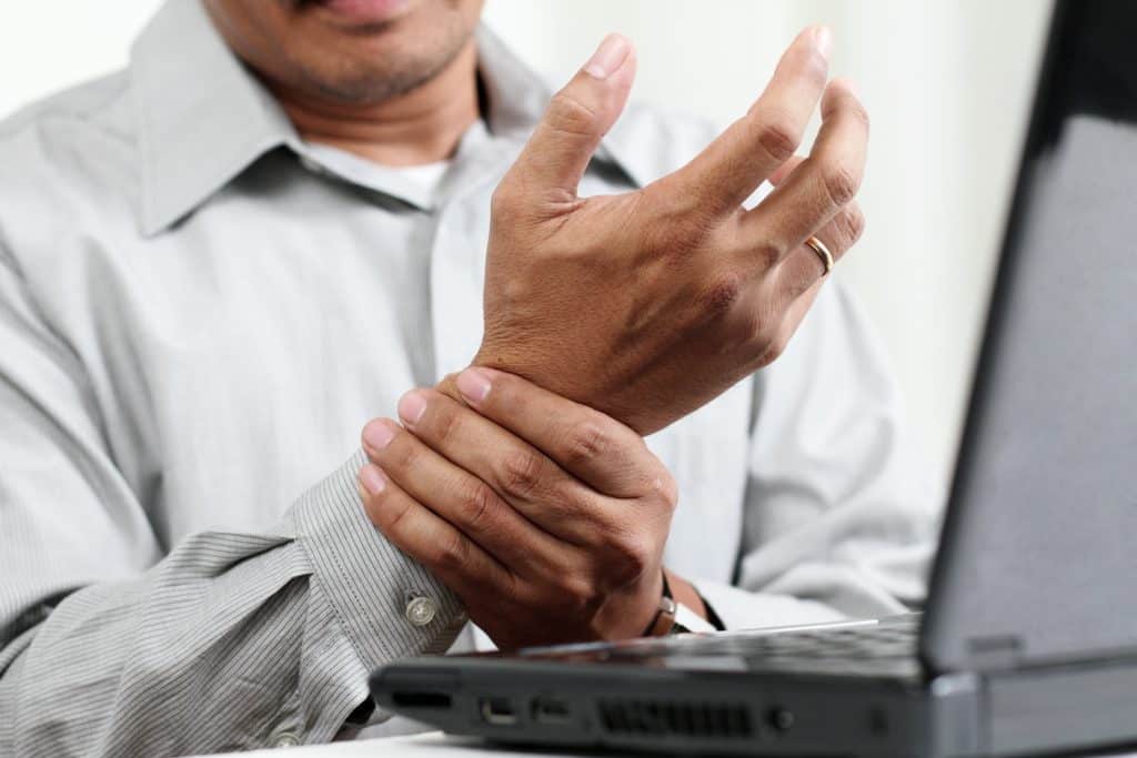 man with carpal tunnel syndrome holding hurt wrist sitting at laptop