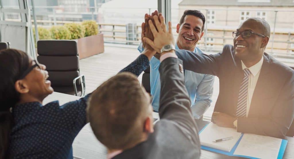 employees around a conference table giving high fives in a happy workplace