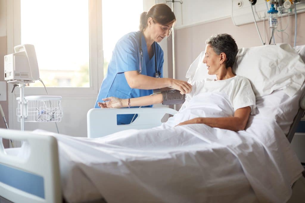 female nurse with PTSD leaning over bedside while attaching the blood pressure armband to a female patients right arm