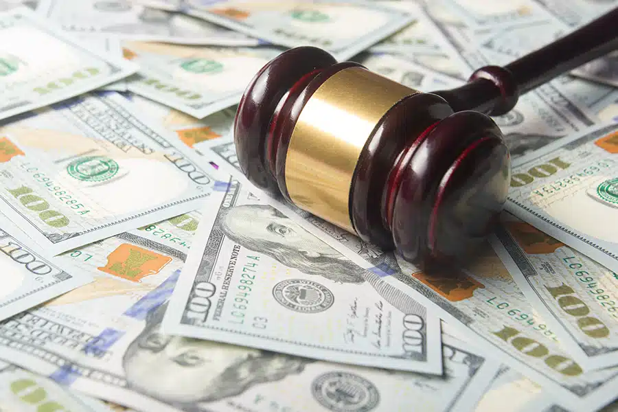 A gavel rests atop a pile of one hundred dollar bills.