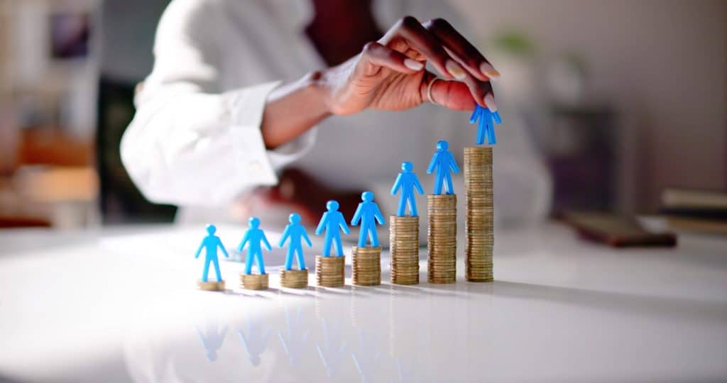 Business woman stacking figurines representing workers on coin stacks of varying heights from smallest to largest