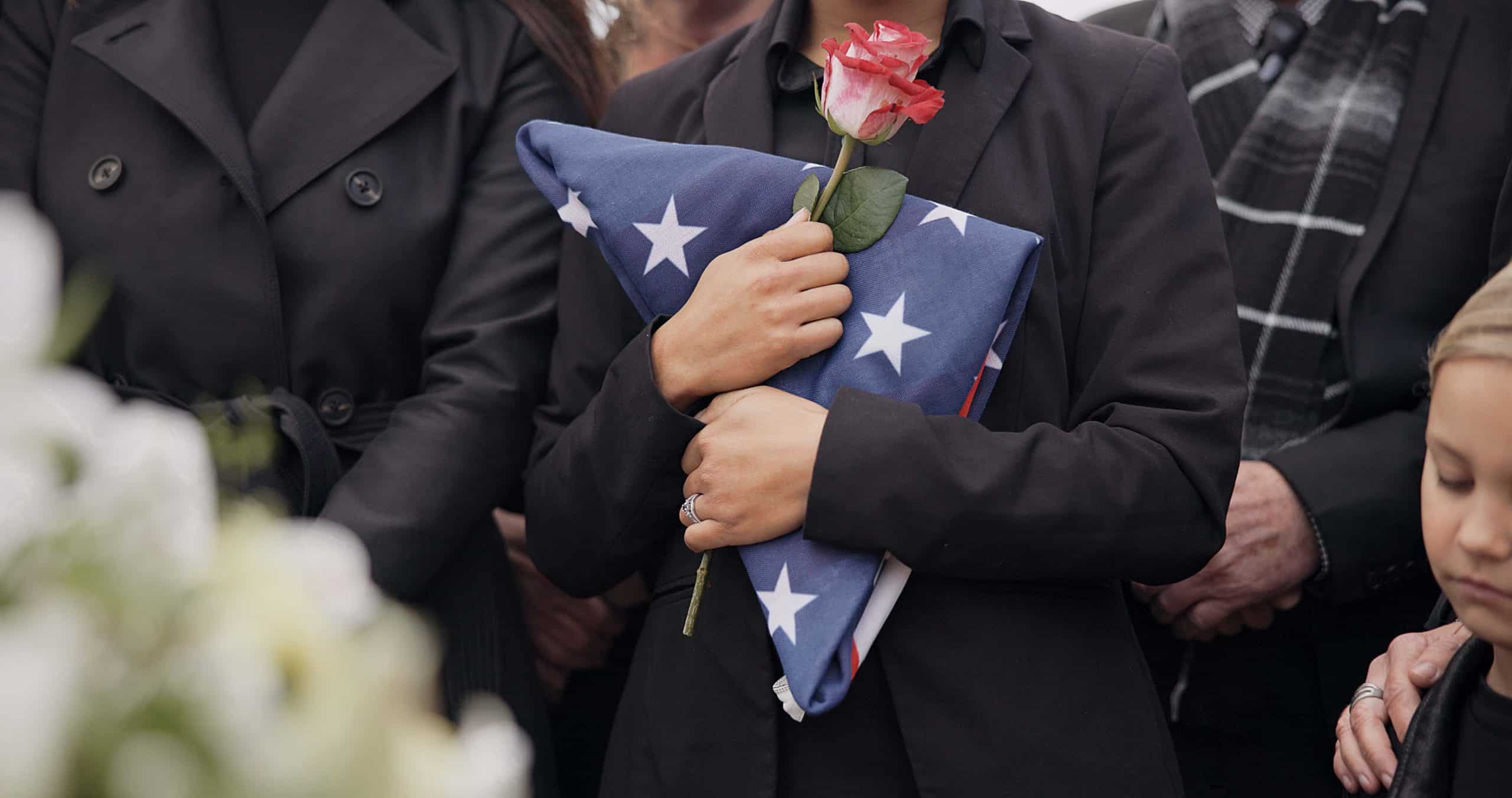 Mourning spouse holds a rose and an American flag.