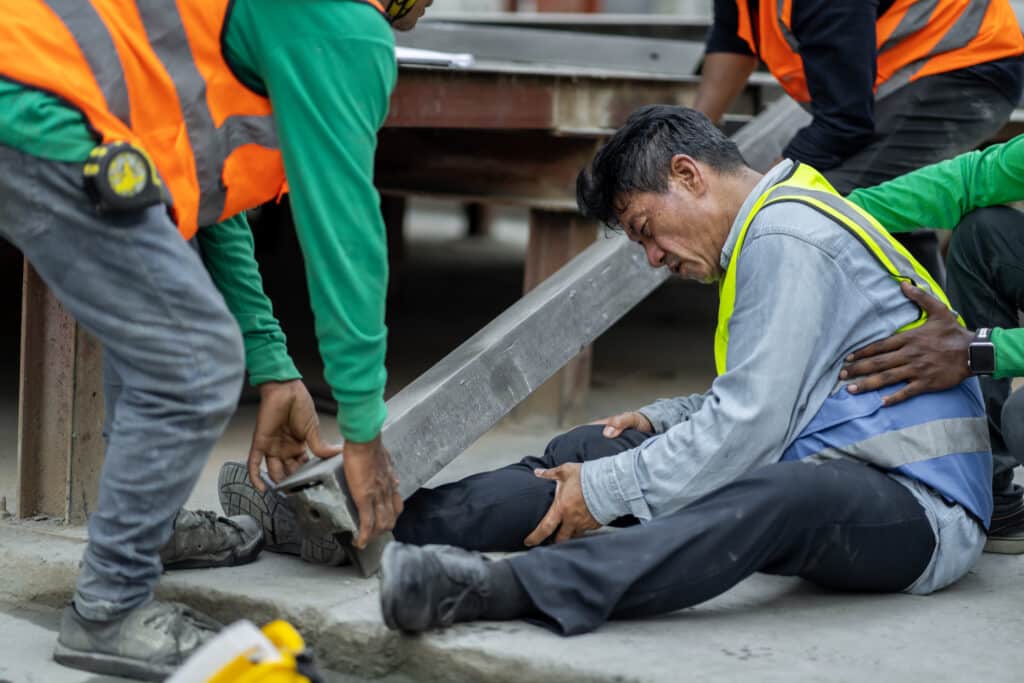 Worker grabs his leg while other workers lift a heavy pole from off the worker