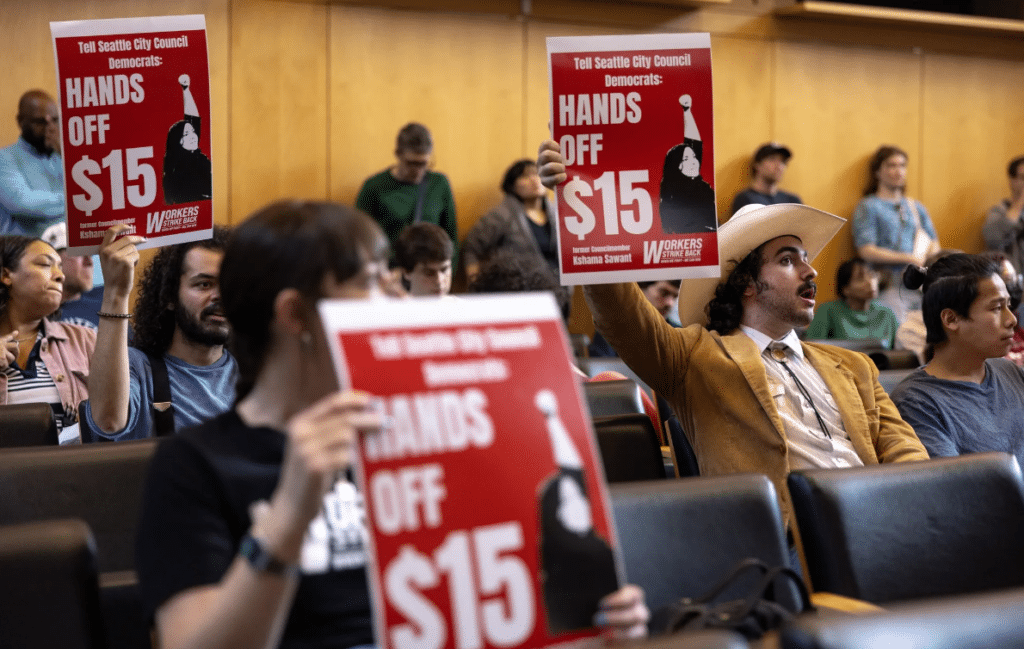 Proponents of protecting Seattle’s minimum wage law hold signs in the council chambers during a public comment period on Tuesday. (Nick Wagner / The Seattle Times)