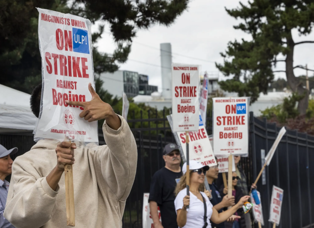  Devon Yann, a quality assurance worker at Boeing for 10 months, points to his sign as he pickets with Boeing Machinist union members and others in front of the Boeing factory in Renton Monday. Yann said he just wants a fair contract for all and is looking out for his future with the company. (Ellen M. Banner / The Seattle Times)